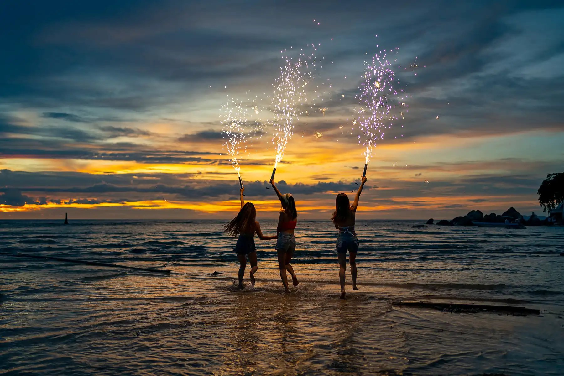 Three women holding fireworks on the beach