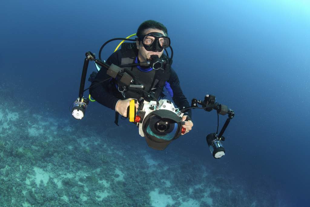 Male scuba diver shooting underwater photography with camera housing, strobes, and lights.