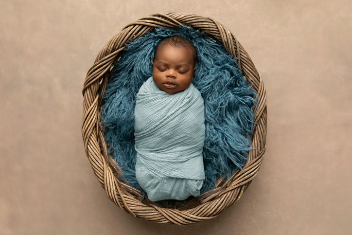 ALT=A classic newborn photography pose is swaddled in a colorful blanket.